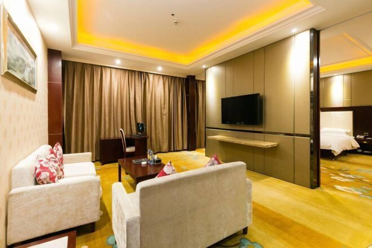 A hotel room with a sofa set, a TV, a desk, and a bed.