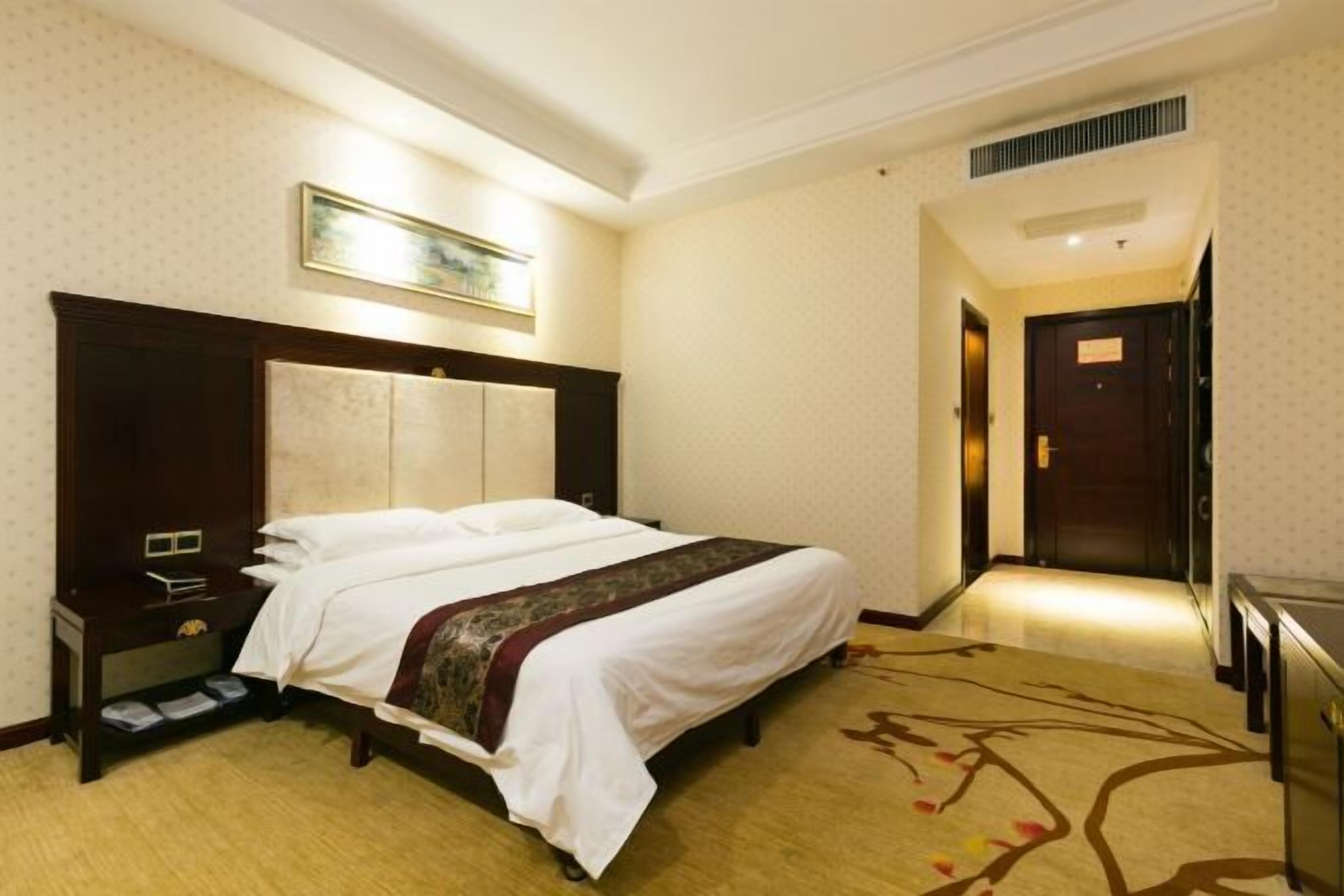 Camera d'albergo con un letto grande, un comodino, una cassettiera e un tappeto con motivo alberi.