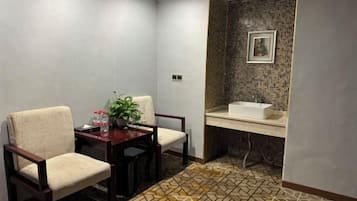 Habitación de esquina con mesa de comedor, dos sillas, una planta pequeña y baño con salpicadero de azulejos y lavamanos.