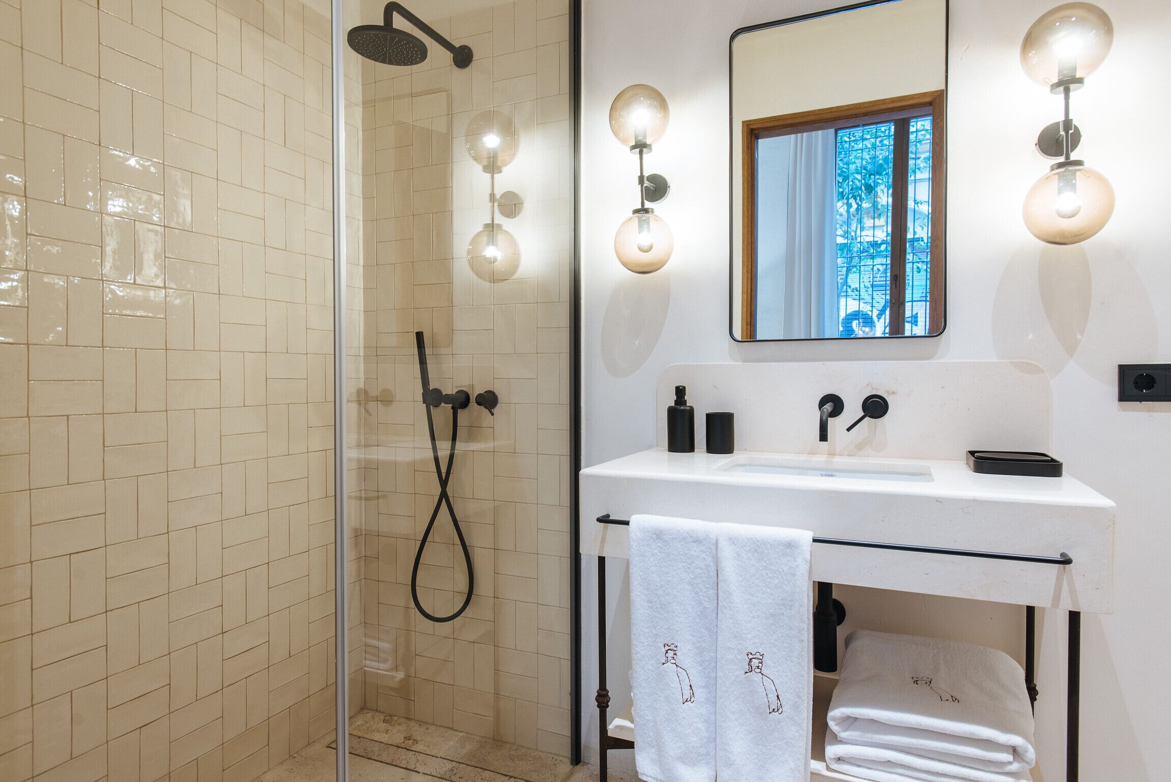 A modern bathroom with a glass-enclosed shower, a white sink with a mirror above it, and wall-mounted lights.