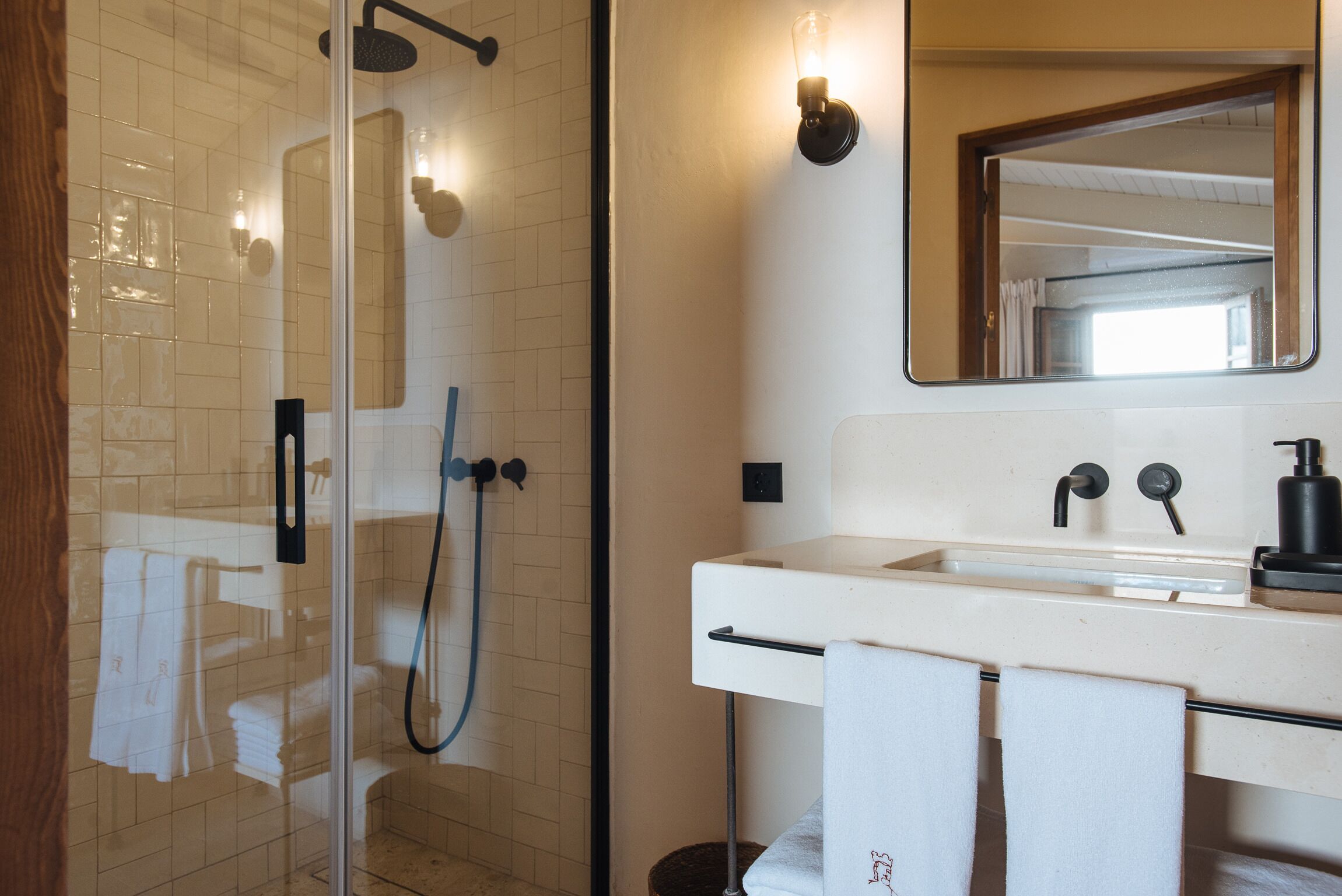 Ein Badezimmer mit einer gläsernen Duschkabine, einem weißen Waschbecken mit Spiegel darüber und Handtüchern, die an der Wand hängen.
