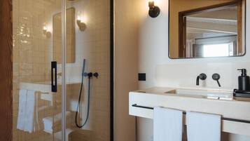 Ein Badezimmer mit einer gläsernen Duschkabine, einem weißen Waschbecken mit Spiegel darüber und Handtüchern, die an der Wand hängen.