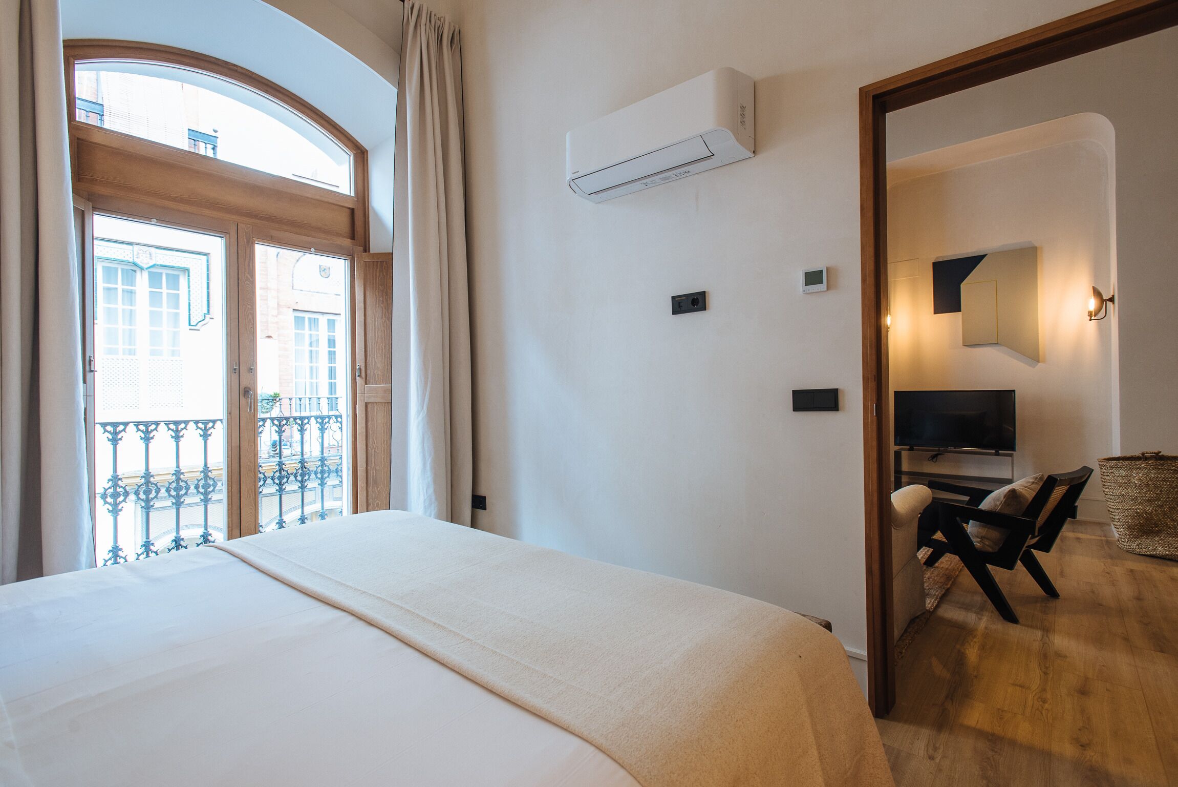 Quarto de hotel com cama, televisão, cadeira e varanda com vista para edifícios.