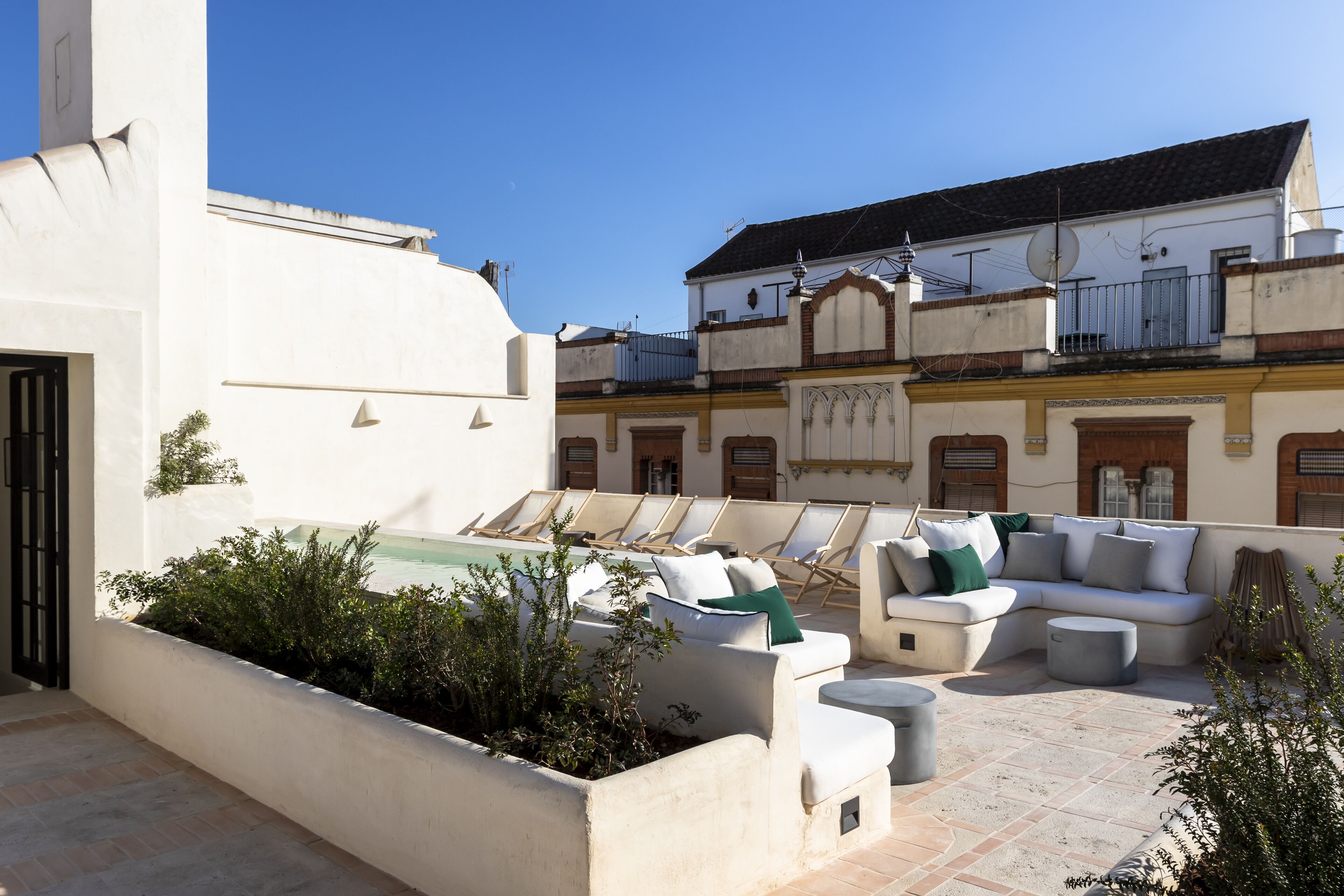 A rooftop terrace with a pool, outdoor seating, and a view of adjacent buildings.