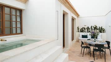 A pool area with steps leading to a white wall, a dining table with chairs, and a sofa with cushions.