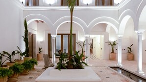 Un vestíbulo espacioso con un jardín interior central, columnas blancas y suelo de baldosas.