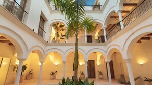 A spacious courtyard with multiple arches, potted plants, and a central palm tree. -  Casa del Rey Sabio (Seville)