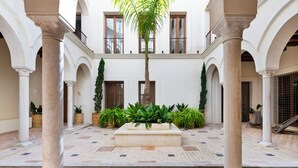 A courtyard with a central water feature, surrounded by columns and potted plants. -  Casa del Rey Sabio (Seville)