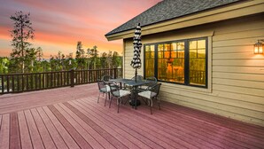 A wooden deck with a table and chairs, a railing, and a building with large windows and a light fixture. - Luxury Home - Incredible Views! Fireplace, Multiple Decks & Hiking from the Property (Grand Lake)