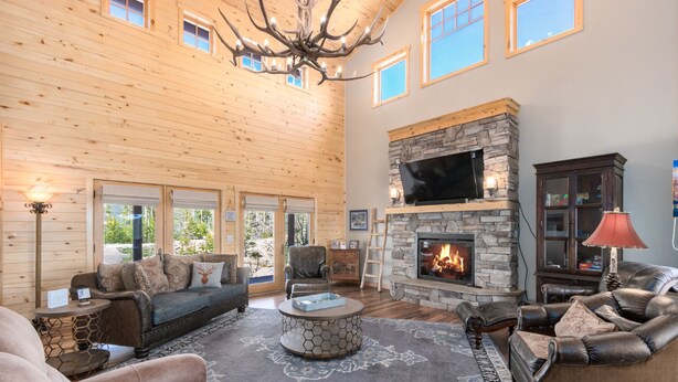 A spacious living room with a stone fireplace, leather sofas, and a chandelier. - Luxury Home - Incredible Views! Fireplace, Multiple Decks & Hiking from the Property (Grand Lake)
