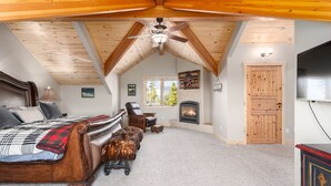 A cozy bedroom with a large bed, a fireplace, and a ceiling fan. - Luxury Home - Incredible Views! Fireplace, Multiple Decks & Hiking from the Property (Grand Lake)