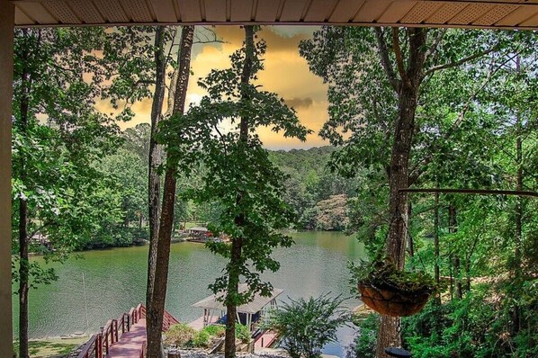A view of a lake surrounded by trees, a wooden deck, and a small dock with a boat.