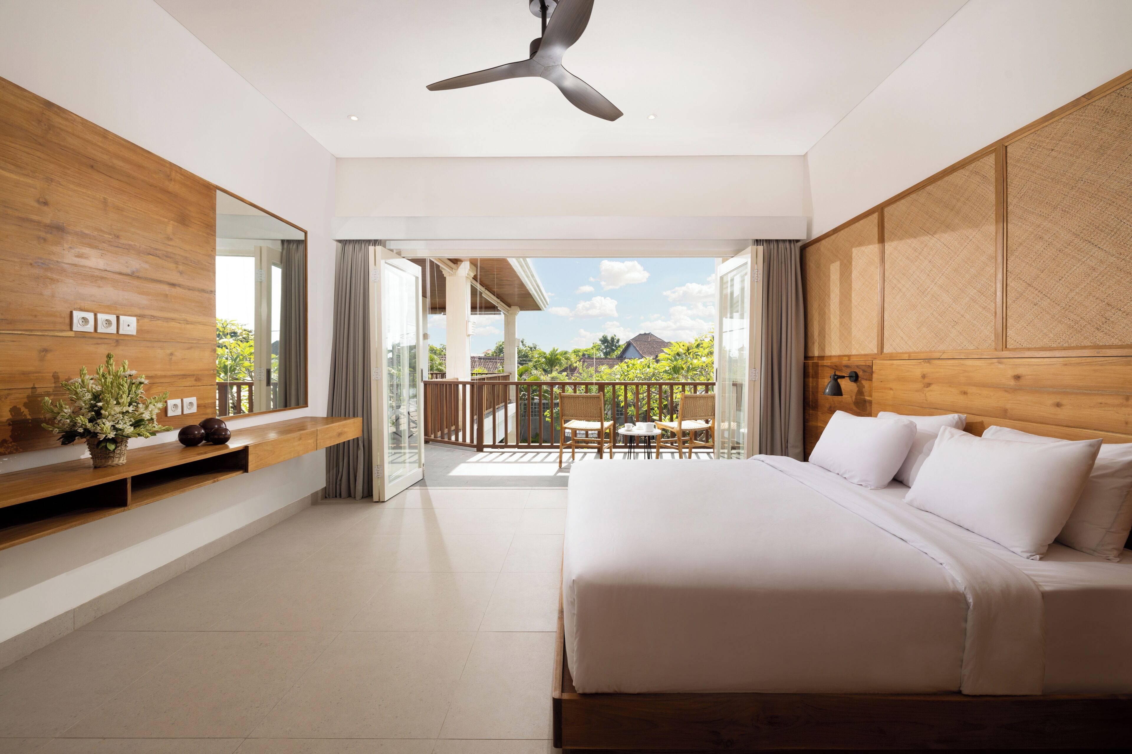 A modern hotel room with a large bed, a balcony with a view, and a ceiling fan.