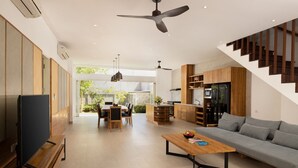 A modern living room with a sofa, coffee table, TV, dining area, kitchen, and staircase. - Villa Christie by Nakula (Seminyak)