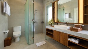 A modern bathroom with a glass-enclosed shower, a white toilet, a marble sink, and wooden cabinetry. - Villa Christie by Nakula (Seminyak)