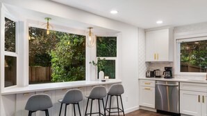 A modern kitchen with white cabinets, a stainless steel dishwasher, and bar stools.