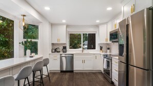 A modern kitchen with white cabinets, stainless steel appliances, and a bar area with stools.