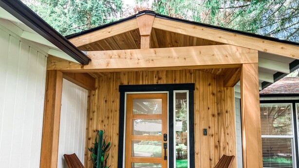A wooden porch with a sliding glass door, two wooden chairs, and a potted plant.