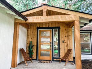 Un portico in legno con una porta a vetri scorrevoli, due sedie di legno e una pianta in vaso.
