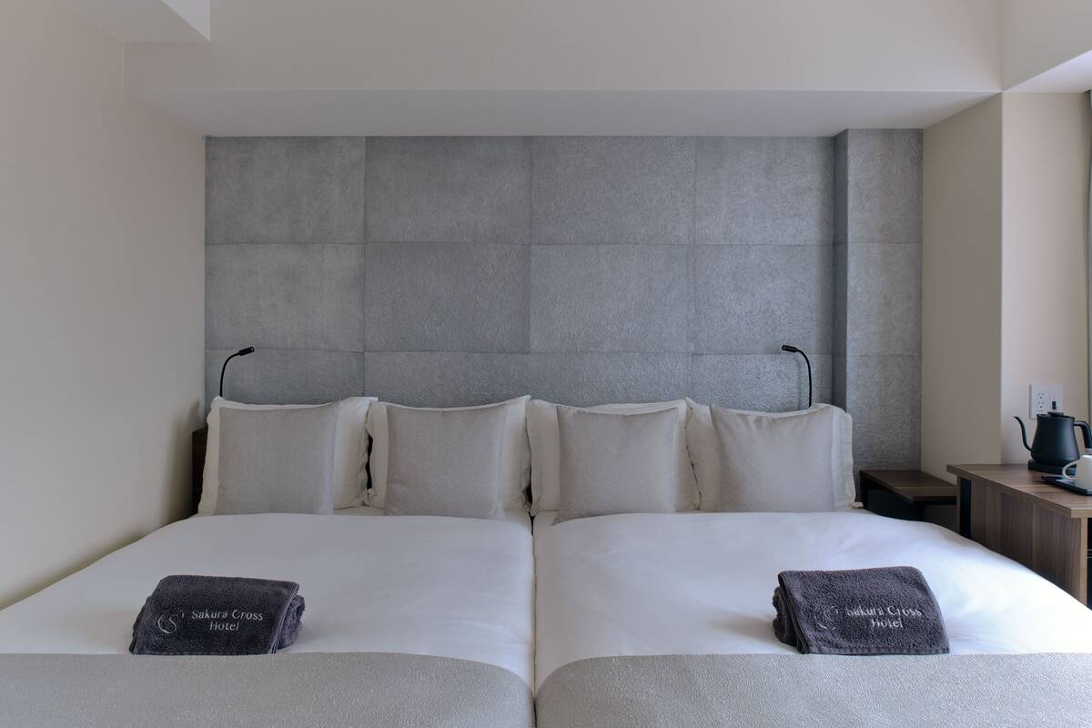A hotel room with a large bed, two pillows, a bedside table, and a nightstand.