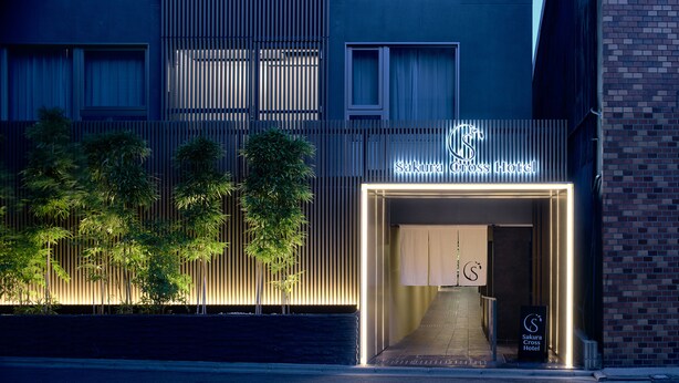 The exterior of Sakura Cross Hotel with a modern facade, vertical wooden slats, and a neon sign.