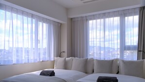 A hotel room with two beds, white bedding, and a view of the city through sheer curtains.