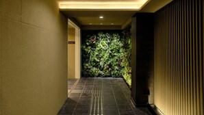 A hallway with a tiled floor, a wall with vertical blinds, and a green wall with plants.