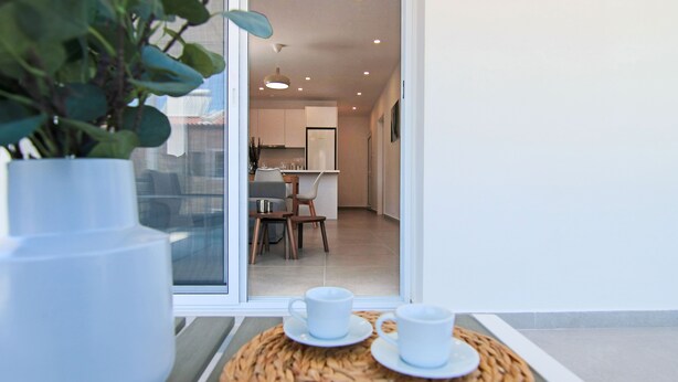 Une cuisine moderne avec des meubles blancs, un coin repas comprenant une table et des chaises, et une grande fenêtre donnant sur l’intérieur.