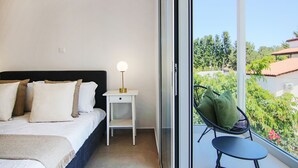 Une chambre à coucher avec un lit, une table de chevet, une lampe et une vue sur la verdure.