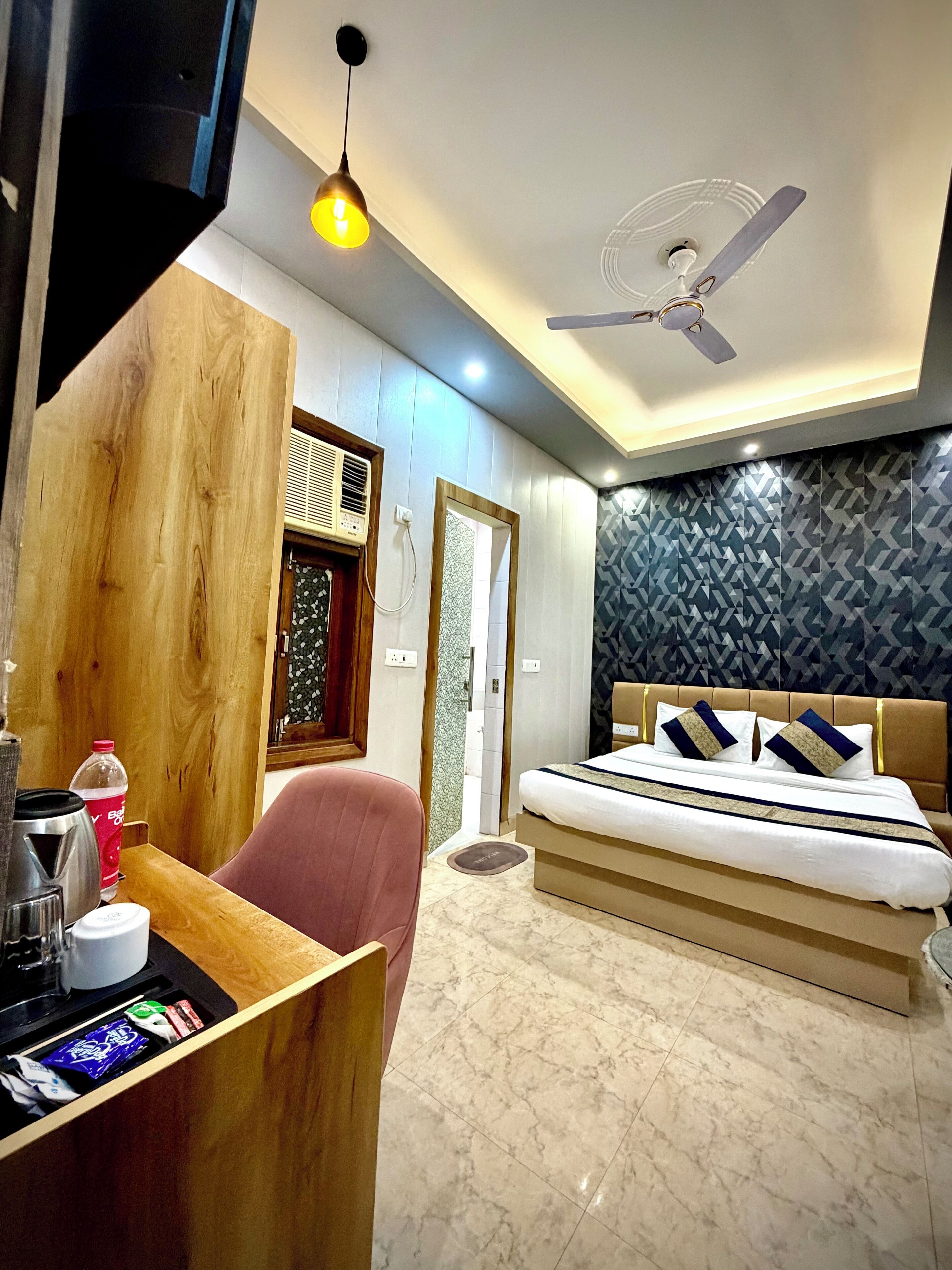 A hotel room with a bed, a desk, a chair, a ceiling fan, and a patterned wall.