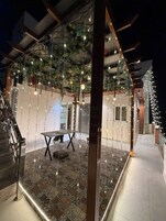 Un espacio interior moderno con piso estampado, una mesa, sillas, luces de cadena y plantas colgantes.