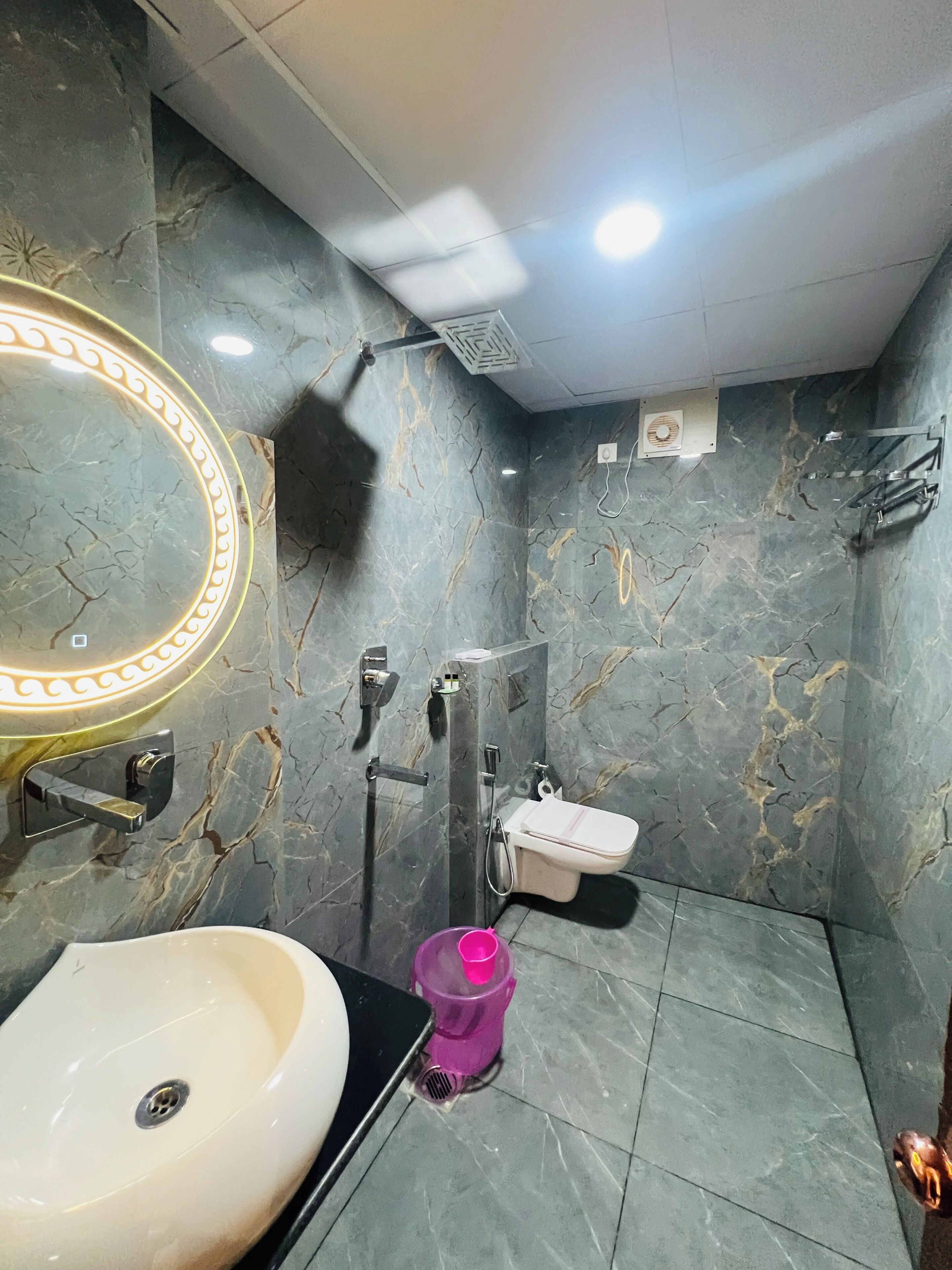 A bathroom with a marble wall, a sink, a toilet, and a shower.
