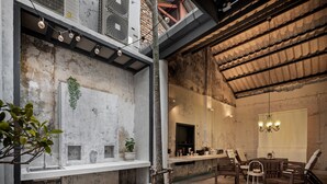Ein modernes Interieur mit einer Betonwand, einer Essecke mit Holztisch und -stühlen und einer hängenden Leuchte.