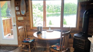 A wooden cabin interior with a dining table, chairs, a fireplace, and a view of a lake.