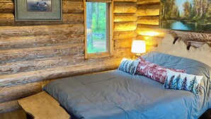 A log cabin bedroom with a bed, a small table, and two windows.