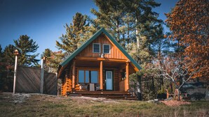 A log cabin with a green roof, a porch with wooden benches, and a clear sky.