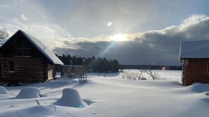 A snowy landscape with two log cabins, one with a visible chimney and another with a Canadian flag.