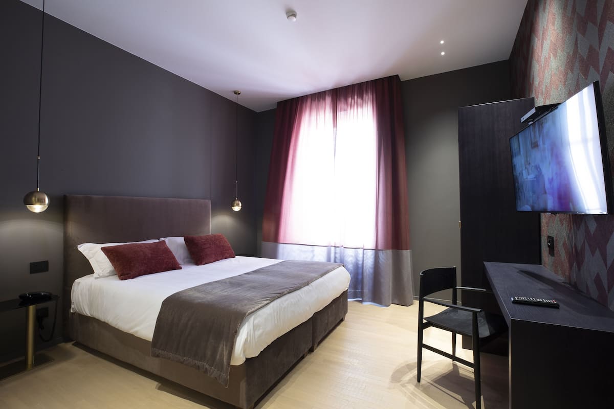 A modern hotel room with a large bed, a desk, and a flat-screen TV.