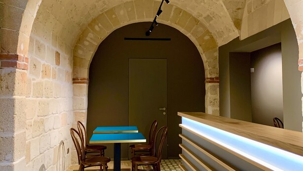 Un interior con una mesa y sillas de madera, un suelo estampado y un mostrador de recepción con iluminación.