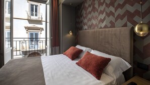 Habitación de hotel con una cama grande, dos almohadas, vistas a un balcón y una pared con diseño.
