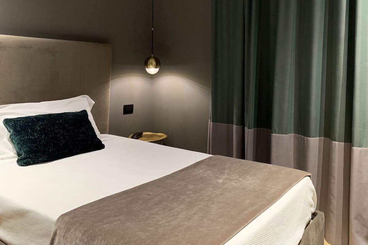 A hotel room with a bed, a bedside table, a lamp, and curtains.