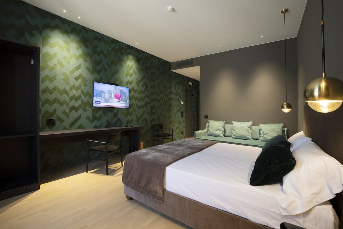 A modern hotel room with a large bed, a desk, and a television on the wall.