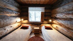 A cabin with two beds, a window with a view of trees, and a small table between the beds. - Rukan Salonki Chalets (Kuusamo)