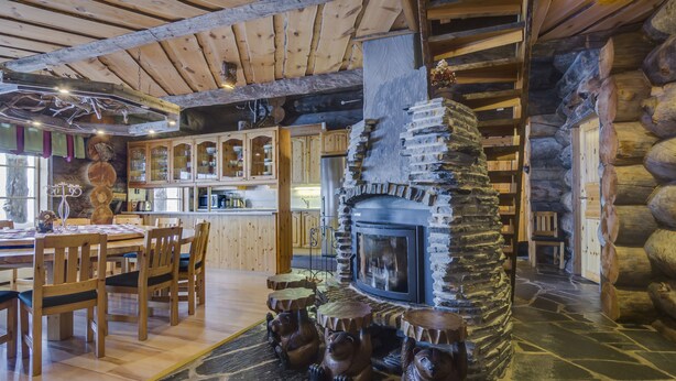 A rustic interior with a stone fireplace, wooden dining table, and chairs. - Rukan Salonki Chalets (Kuusamo)