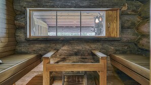 A log cabin room with a wooden bench, a window with a view of a tree, and a wooden table. - Rukan Salonki Chalets (Kuusamo)
