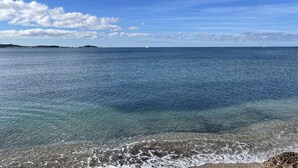 Küstensicht mit klarem Wasser, einem Sandstrand und entfernten Landformen.
