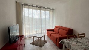 A small living area with a red sofa, a TV on a red cabinet, a small table, and a window with sheer curtains. - Family studio near slopes, parking, Villard-de-Lans (Villard-de-Lans)