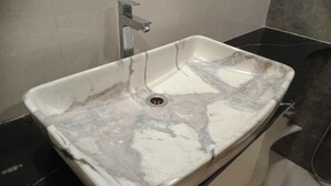 Une salle de bain avec un lavabo en marbre, un robinet moderne et un plan de toilette noir.