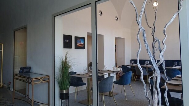 A modern office space with glass partitions, a reception desk, and a dining area with blue chairs and a plant.