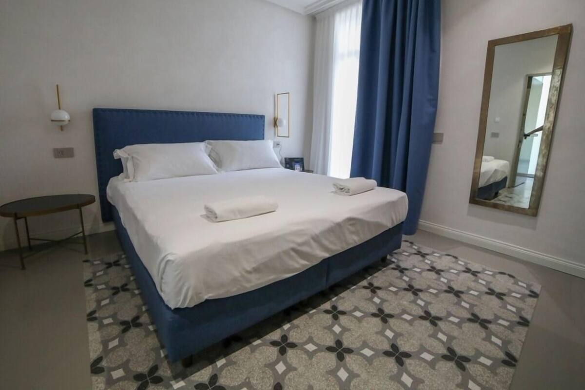 A neatly made bed with white linens, a blue headboard, and a small bedside table with a lamp.